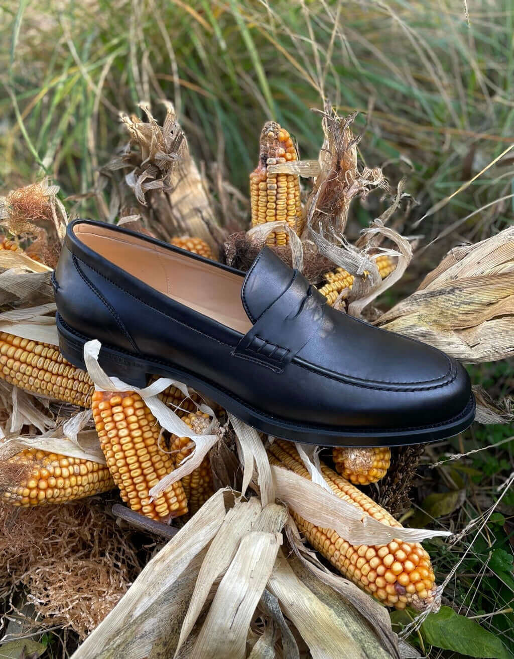 What is Vegan Leather? Stylish black loafers displayed on dried corn husks in a natural setting.